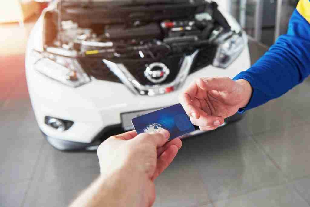 Hands of car mechanic with wrench in garage, payment by credit card